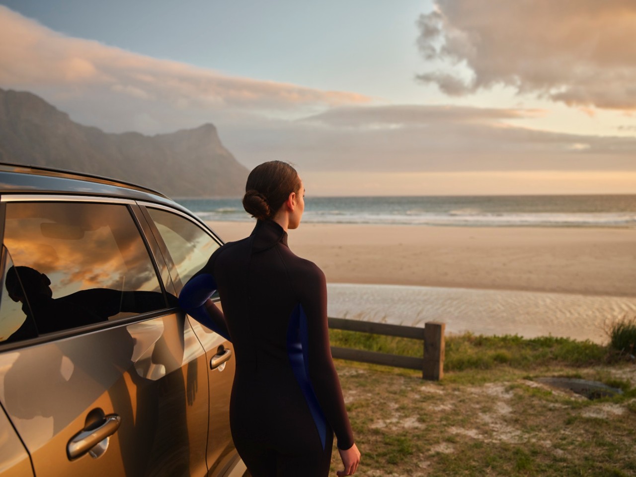 Woman stood next to Toyota bZ4X at sunset