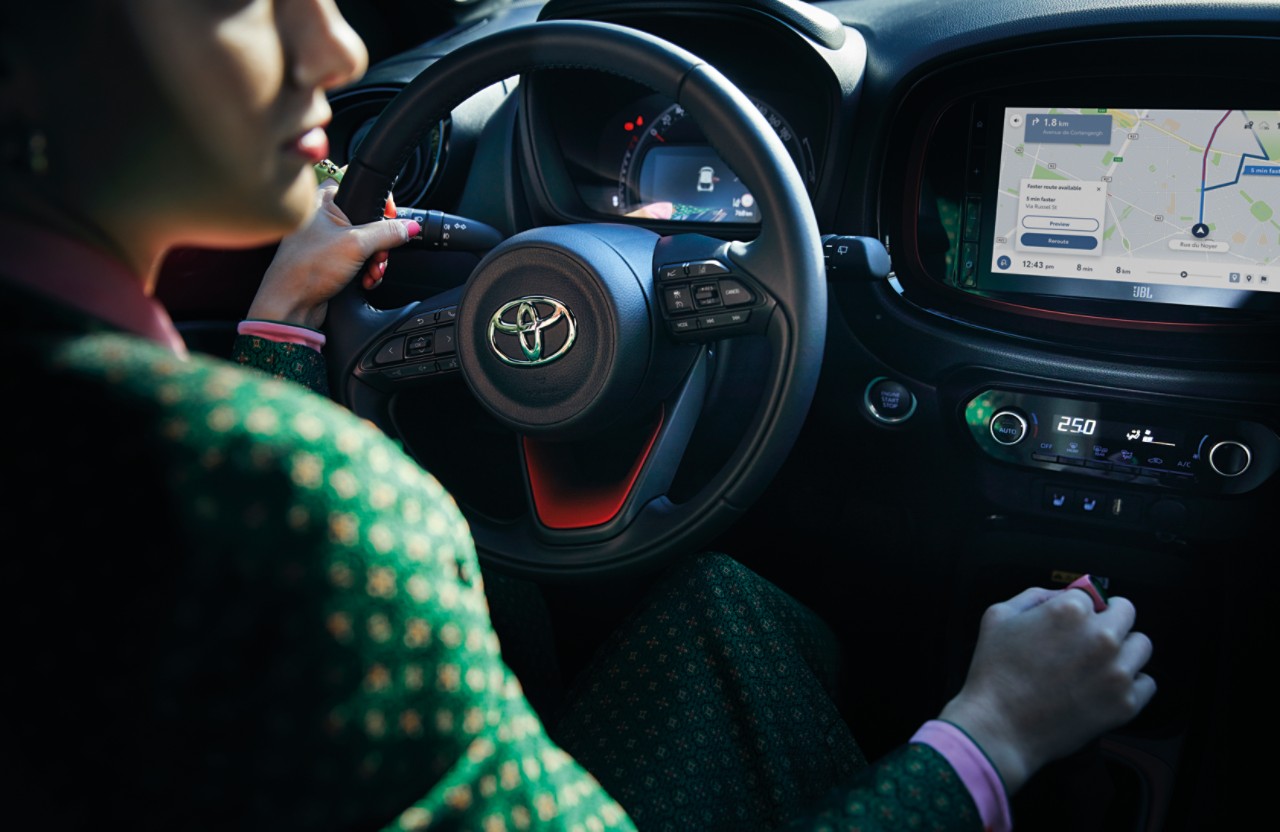 Woman in green suit driving Toyota Aygo X
