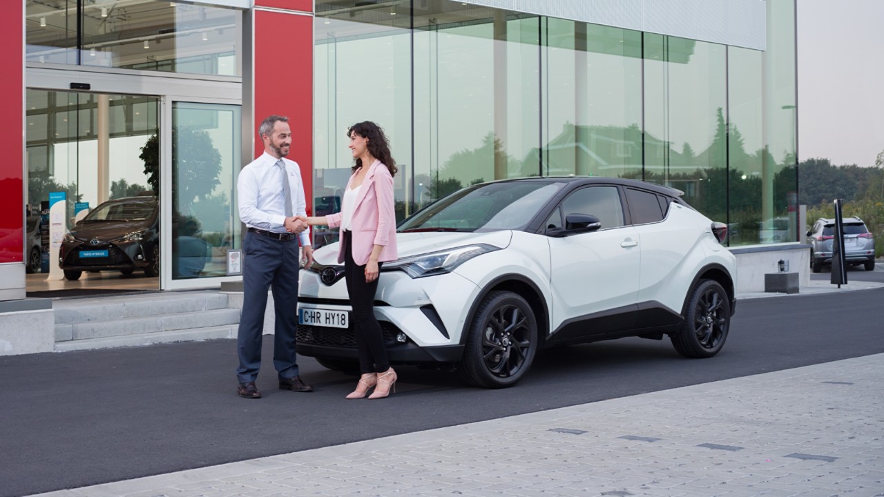 two people shaking hands next to a Toyota car