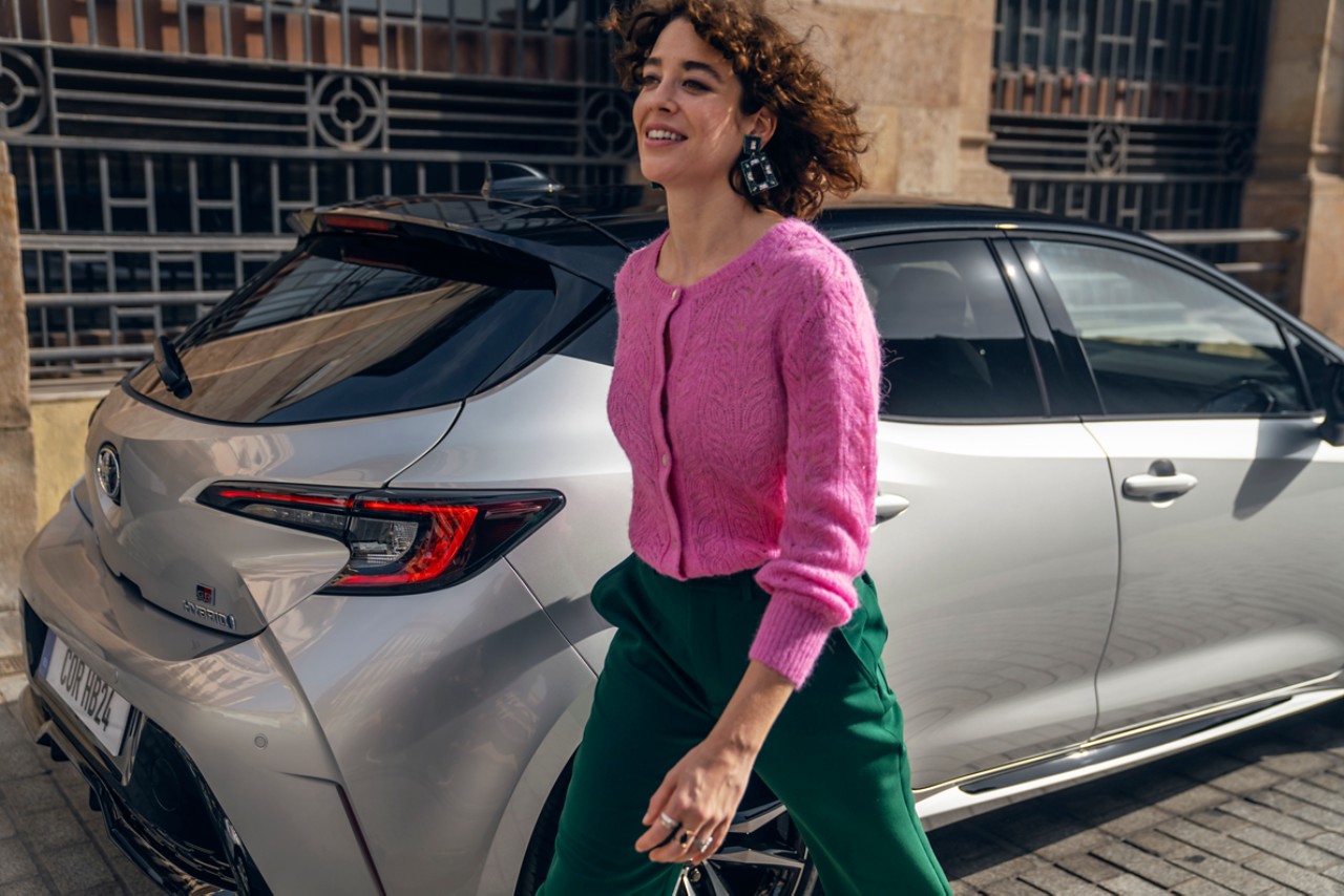 woman smiling and walking past Toyota Corolla