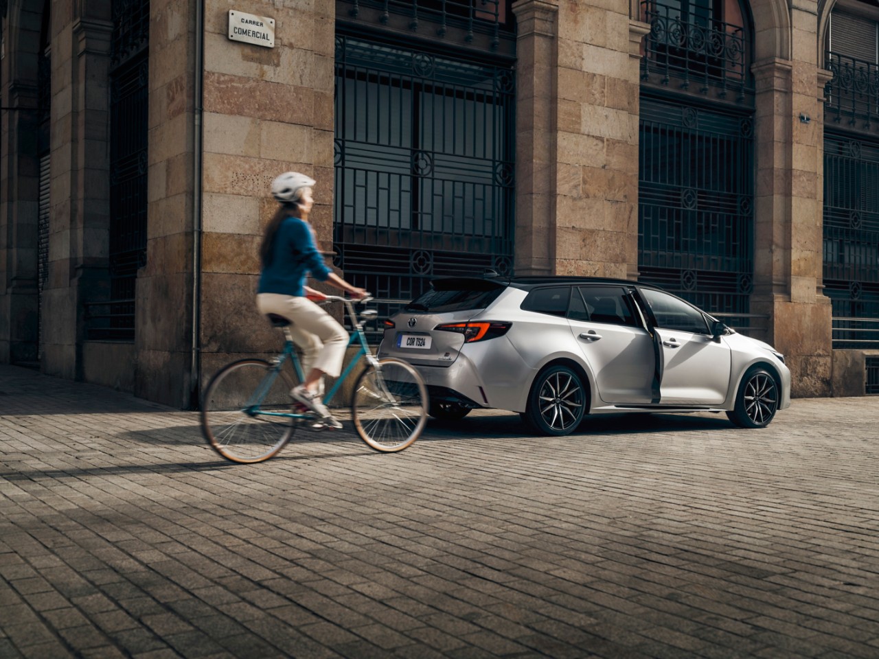 Woman biking by Toyota Corolla Touring Sports parked