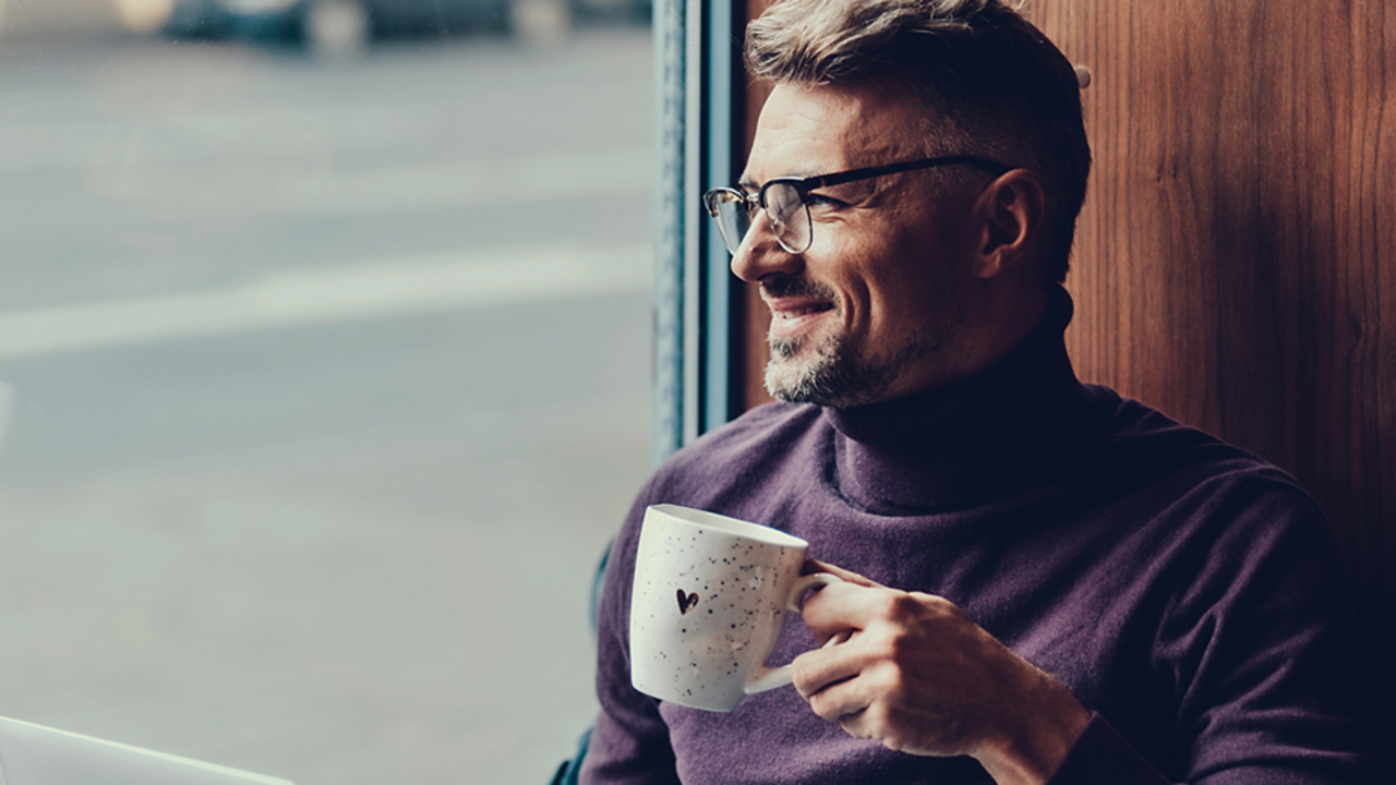 Man smiling looking out window holding mug